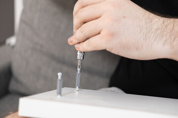 Male hand utilizing a screwdriver to assemble white flat-pack furniture, symbolizing home improvement, practical repair, and do-it-yourself project completion