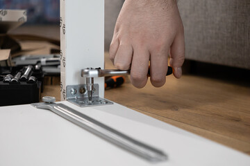 Close-up of hand assembling modern white modular furniture with a ratchet screwdriver, fastening a metal bracket, representing practical home improvement and DIY work