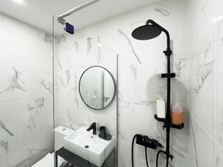 modern bathroom showcases a black shower system against white tile walls. The shower features a rainfall head and handheld sprayer, creating a sleek contrast