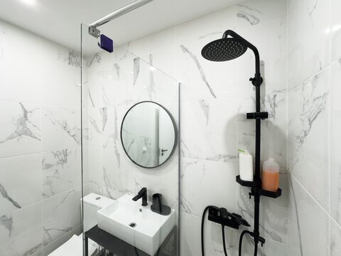 modern bathroom showcases a black shower system against white tile walls. The shower features a rainfall head and handheld sprayer, creating a sleek contrast