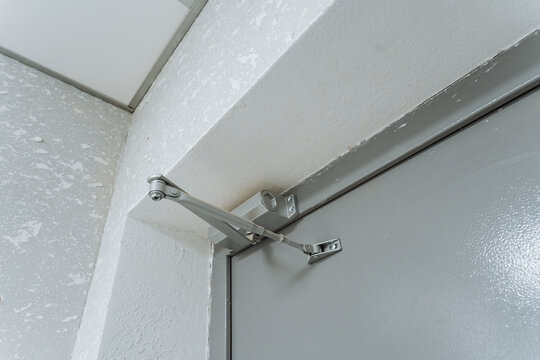 door hardware components, metal door closer with adjustable arm, entryway door mechanism featuring bolts and hinge details, adjustable arm door closer mounted on metallic frame with hardware details