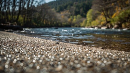 Fototapeta premium River scene with pebbled shoreline, flowing water, trees, and hills in the background. Nature and outdoor landscape.