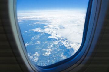 Aerial view of clouds and landscape from airplane window on sunny day