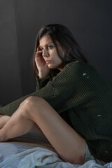 Fototapeta premium A sad woman sits on a bed, head bowed, wearing a worn sweater. Her pose conveys a sense of emptiness and intense emotional pain, and the soft lighting adds a sense of vulnerability