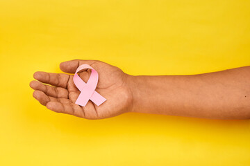 A hand presenting a pink ribbon representing awareness support and hope in the global fight against breast cancer.
