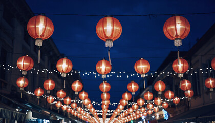 Red Chinese lanterns strung across a street at dusk with small white lights nigh.