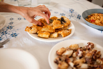 Hand Reaching for Fried Fish on Rustic Table with Seafood Dishes