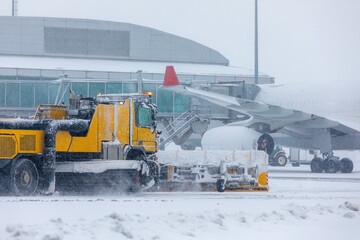 Special snow plow truck along airport runway during heavy snowfall. Scene shows airplane delay and winter maintenance in harsh weather.