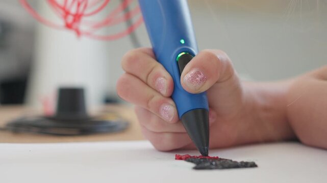 3D pen closeup of girl creating plastic 3D model, drawing. Unknown child's hand draws with pen on paper at table. Technology. Robotics. STEM education