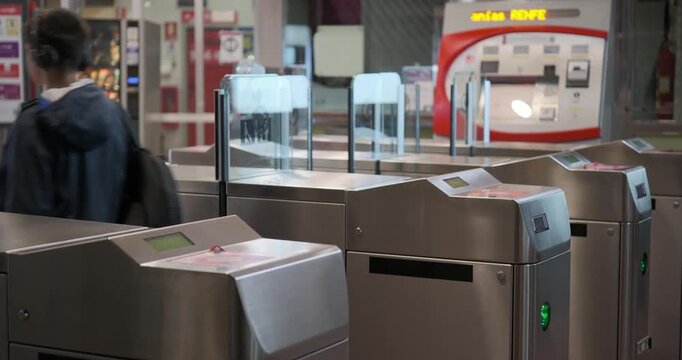 Rear view of a teenage boy with headphones walking through the ticket turnstiles at a subway or railway station during his daily commute.