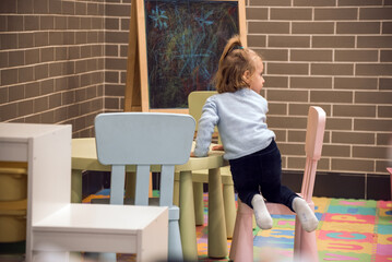 A young girl is sitting on a pink chair in front of a chalkboard