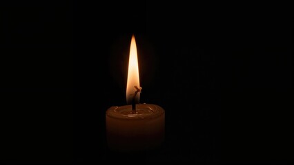 A single lit candle with a flame burning in an otherwise dark environment.