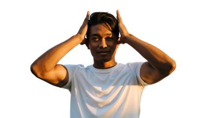 Close-up portrait of a young man with hands on head, bathed in warm outdoor light.