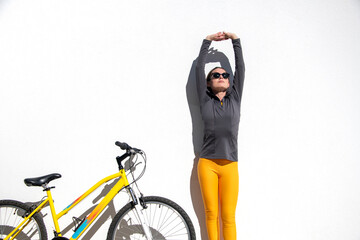 sporty woman standing stretching by a yellow bicycle