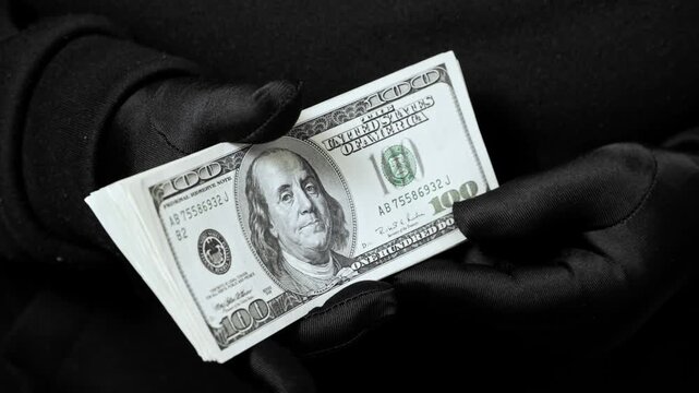 Hands gripping dollar notes. Close-up of US paper money held firmly. Cash flow, budgeting, and personal finance made tangible. Dark background draws attention to the notes.