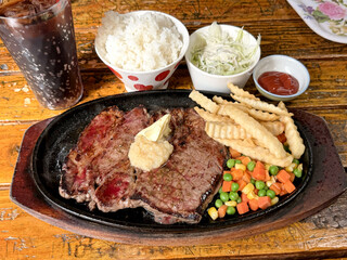 Juicy grilled steak served with french fries, rice, and mixed vegetables on a sizzling platter