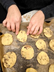 Children's hands placing homemade chocolate chip cookies on a baking sheet