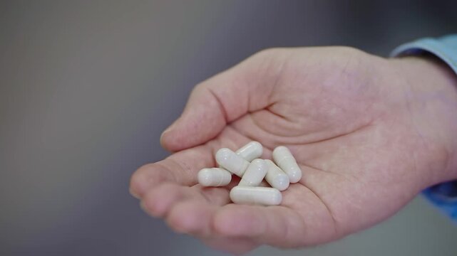 Close-up of a man&rsquo;s hand holding many pills poured from a medicine jar. Home setting. Healthcare and medication use. Visual warning about overdose risk, misuse of drugs, and the importance of medical 