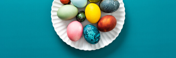 Festive, colorful eggs in various shades are neatly arranged on a decorative plate, symbolizing Easter traditions and spring celebrations with vibrant designs, banner