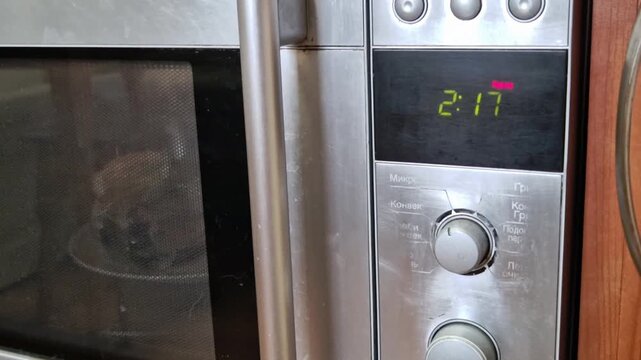 Close-up of a stainless steel microwave oven with its digital timer counting down. Green numbers on the black display reflect the modern kitchen appliance's function and show time remaining.