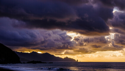 Dramatic cloudy sky over the ocean during sunset with silhouetted mountains.