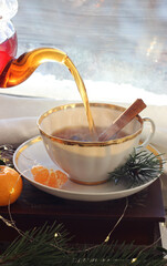 Tea from a transparent teapot is poured into a mug near the window. New Year's atmosphere