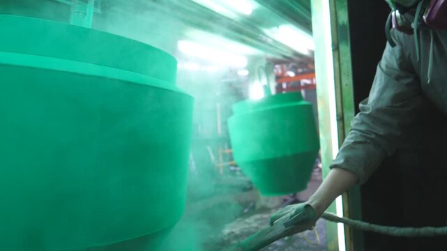 Worker spraying green paint on detail in painting chamber. Painter working at industrial manufacture. Master paint detail in specialised workshop. Man painting parts in production. Slow motion Closeup
