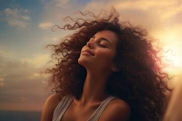 Woman enjoying sunset by the ocean with curly hair flowing freely and a blissful expression on her face