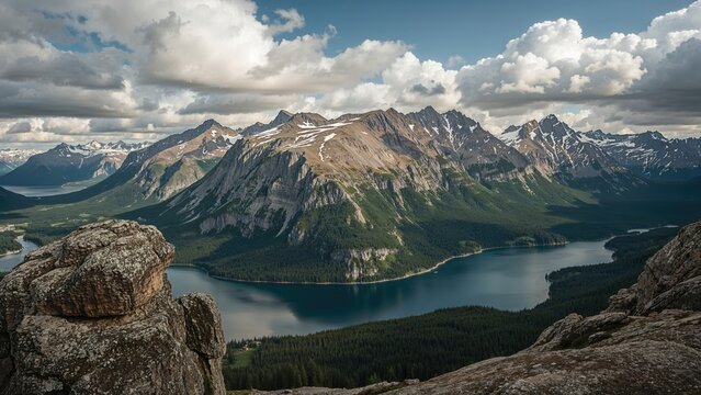 Scenic mountain landscape with a lake, rugged peaks, and cloudy sky, viewed from a rocky vantage point.