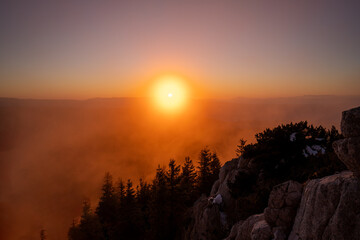 Mountain Sunset With Trees, Rocky Cliffs and Soft Clouds Over Distant Peaks