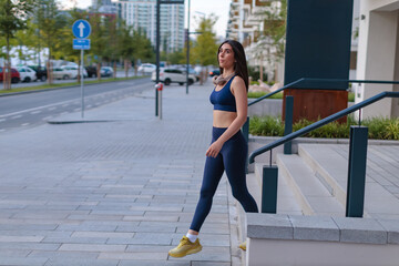 Woman walks on sidewalk in city wearing workout clothes during morning