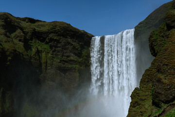 Powerful Sk&oacute;gafoss waterfall falling down a mossy cliff under a clear blue sky
