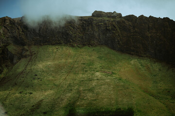 A dramatic rocky mountain in South Iceland is illuminated by soft sunlight and surrounded by green meadows. Minimalistic and moody Icelandic landscape
