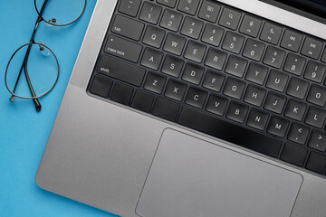 Laptop keyboard and eyeglasses on blue desk