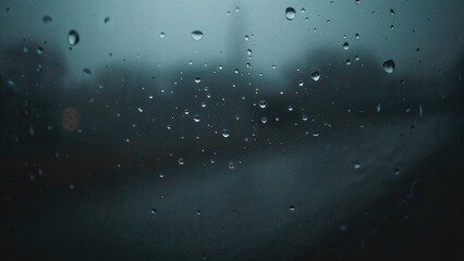 Obraz premium Rainy window with water droplets, gloomy weather, and blurred background. Weather and rain scene. The atmosphere of a rainy day through a glass surface.
