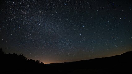 Fototapeta premium A clear night sky with stars and the Milky Way above a silhouetted landscape. Night sky view with stars and cosmic phenomena at nighttime.