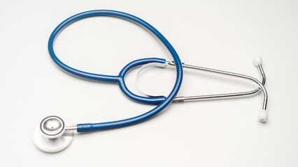 A blue stethoscope is laying on a white background. The stethoscope is a medical instrument used to...
