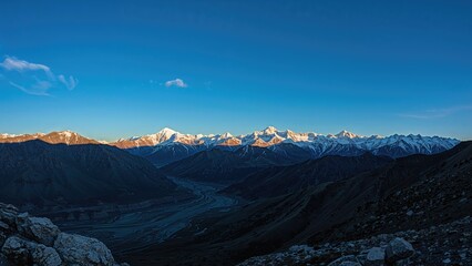 Naklejka premium Snow-capped mountains from a distance with a deep valley below under a clear sky. Landscape of remote wilderness and rugged terrain.