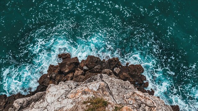Rocky cliff overlooking ocean with crashing waves. Nature, coast, and seascape scene. - Powered by Adobe