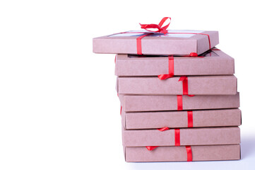 A clean and modern holiday-themed image showing a stack of kraft gift boxes tied with bright red satin ribbons. The white background emphasizes the simplicity and elegance of the arrangement.