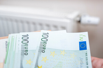 Euro banknotes in hand emphasizing currency and financial transactions in domestic settings. Close-up shot against a blurred background of a radiator.