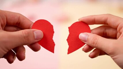 Hands holding torn red paper heart, symbolizing broken love and relationship end