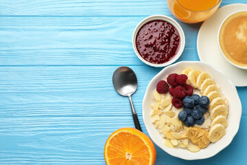 Healthy breakfast. Oatmeal with nuts, banana, berries, jam, coffee and juice served on light blue wooden table, flat lay. Space for text