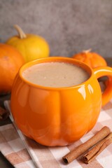 Warm pumpkin latte, cinnamon sticks and fresh vegetables on wooden table, closeup