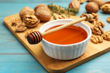 Honey in bowl, dipper and walnuts on light blue wooden table, closeup