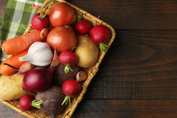 Different raw vegetables in basket on wooden table, top view. Space for text