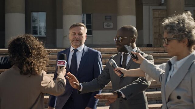 Medium shot of African American male bodyguard pushing away eager journalists while accompanying Caucasian lawyer or politician, refusing interview and walking away from court hall after case hearing