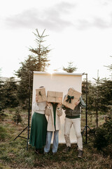 Familie steht in der Natur vor einem beigen Studiohintergrund und versteckt sich hinter Geschenken