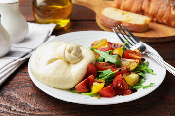 Delicious burrata cheese with tomatoes and arugula served on wooden table, closeup