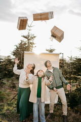 Familie steht in der Natur vor einem beigen Studiohintergrund und wirft Geschenke in die Luft
